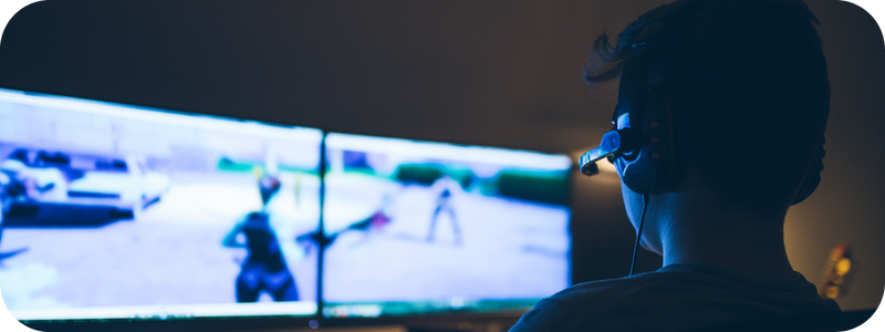 A young male with a headset playing video game on a dual screen computer