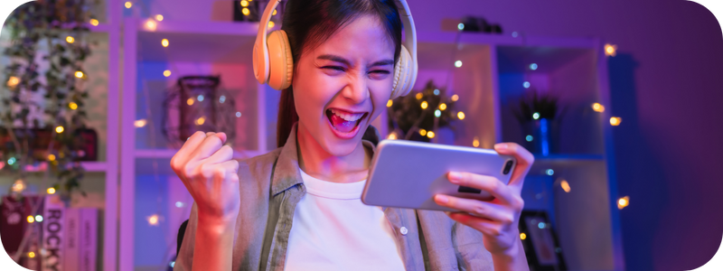 A young woman with headphones cheering while looking at her smartphone
