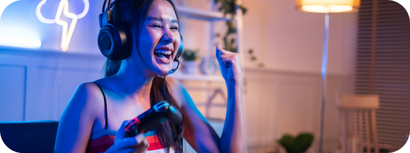 A teenager wearing headsets sitting on a couch with a game console, cheering