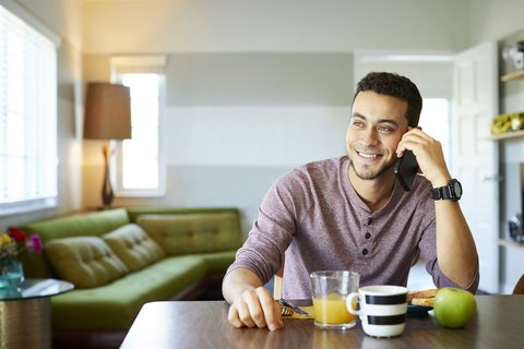 A young male talking on his smartphone at the dining table