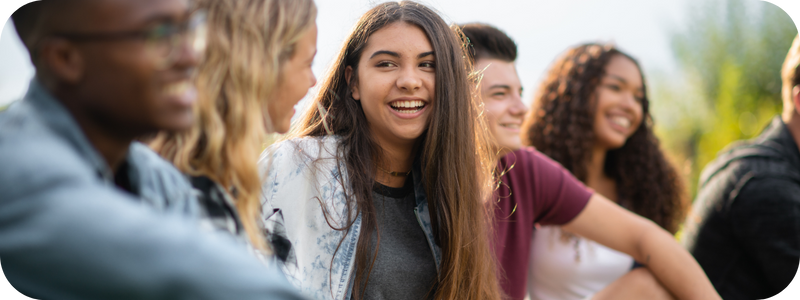 Diverse group of cheerful young people seated together outdoors.