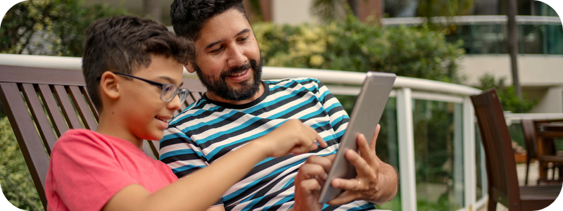 A young boy and his dad outdoors looking at a tablet