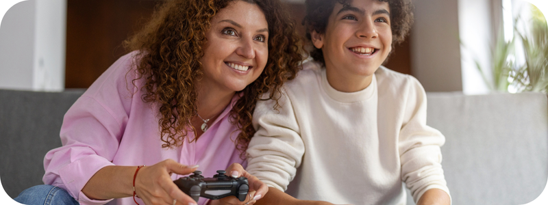 A woman smiling while holding a gaming console seated beside a young male