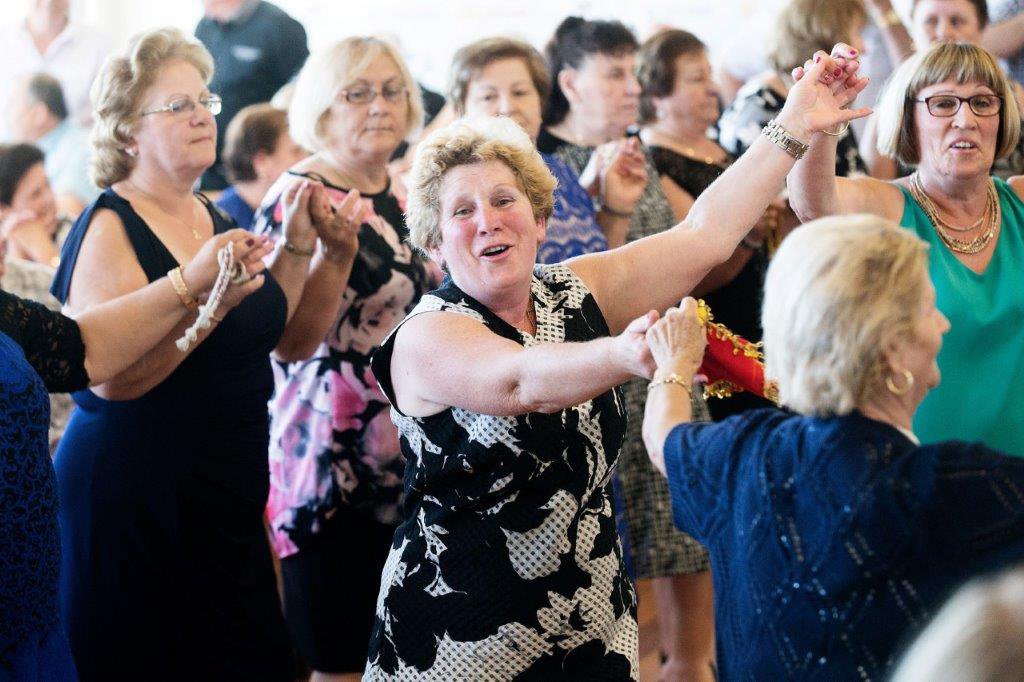 A smiling older woman, hands joined with other women, dancing