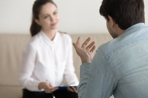 A man and a woman are facing one another, having a conversation. The woman is holding a pen and notepad.