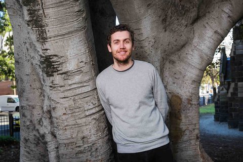 Daniel leans against a huge tree in a church yard and smiles at the camera