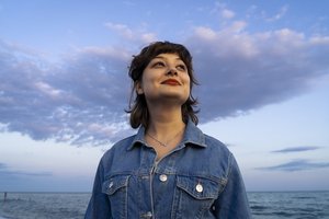 A young woman in denim jacket looking ahead with a smile